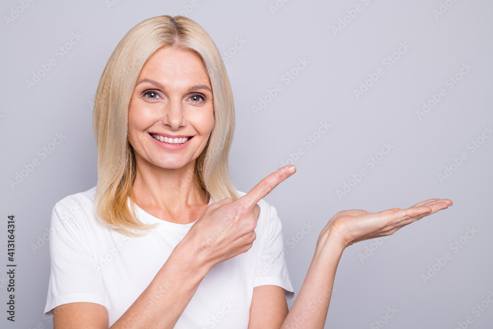 Photo portrait of old woman holding in hand pointing finger at blank space isolated on grey colored background Photo portrait of old woman holding in hand pointing finger at blank space isolated on grey colored background