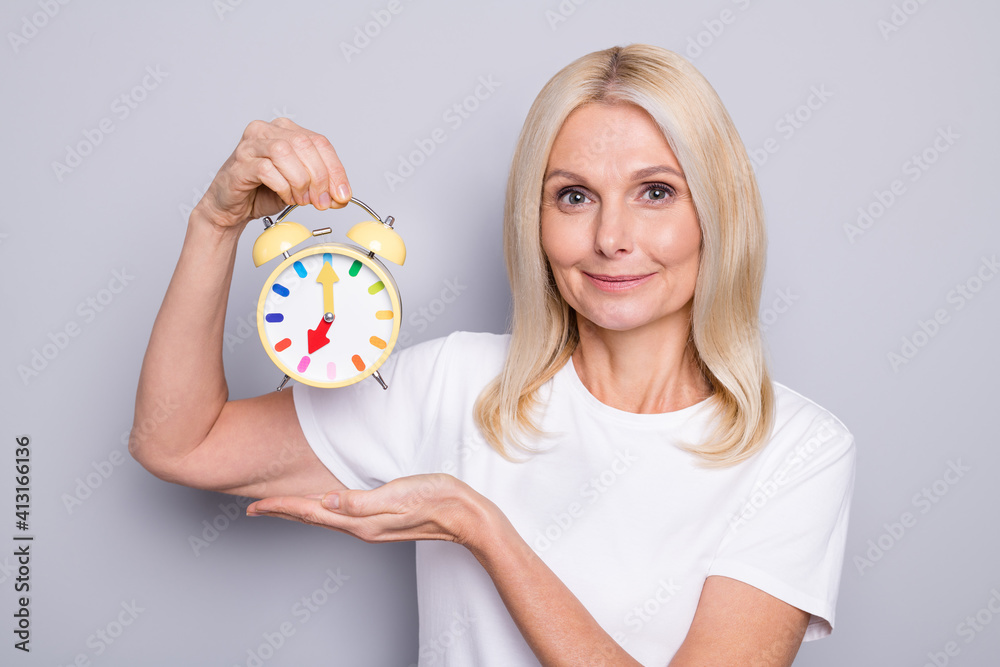 Portrait of blond optimistic old lady show clock wear white cloth isolated on grey color background Portrait of blond optimistic old lady show clock wear white cloth isolated on grey color background