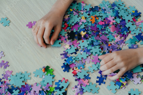 Caucasian girl collects puzzles on the table. Hands of a girl, top view