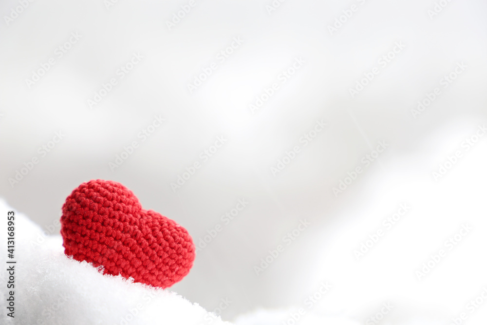 Fototapeta premium Love heart in the snow, background for Valentine's day card with blurred copy space. Red knitted symbol of romantic love