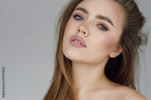 The face of a young beautiful girl with natural makeup, beauty portrait. Clear skin and an expressive look on the girl's face, on a gray background.