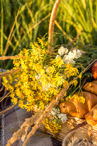 Picnic basket with croissants food and a bouquet of wild flowers photo