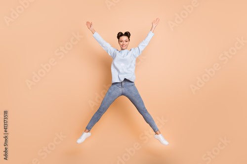 Full size photo of optimistic nice brunette lady jump wear light blue sweater jeans sneakers isolated on beige color background