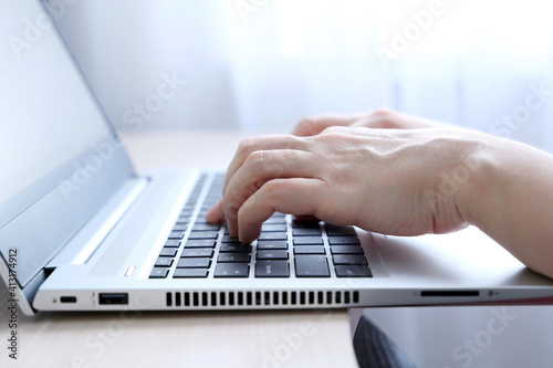 Female hands on laptop keyboard on a desk in sunlight. Woman types on the laptop keyboard sitting near the window, office or home work photo