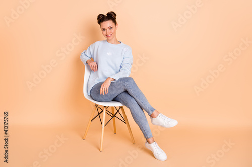 Full size photo of optimistic brunette lady sit wear sweater jeans sneakers isolated on pastel beige color background