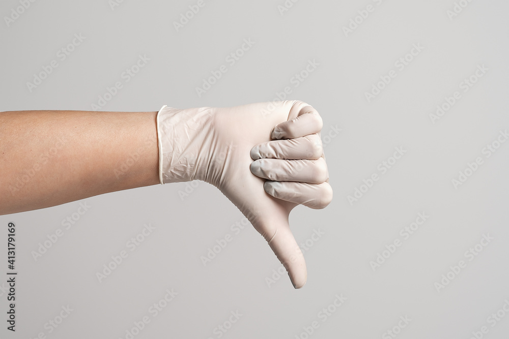 Closeup of the hand in a white sterile glove showing thumb down, isolated over grey background Closeup of the hand in a white sterile glove showing thumb down, isolated over grey background
