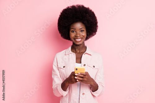 Portrait of lovely cheerful wavy-haired girl influenzer using gadget post smm isolated over pink pastel color background