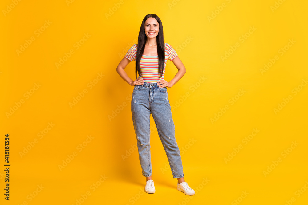 Full size photo of young happy cheerful smiling good mood girl in jeans and striped t-shirt isolated on yellow color background Full size photo of young happy cheerful smiling good mood girl in jeans and striped t-shirt isolated on yellow color background