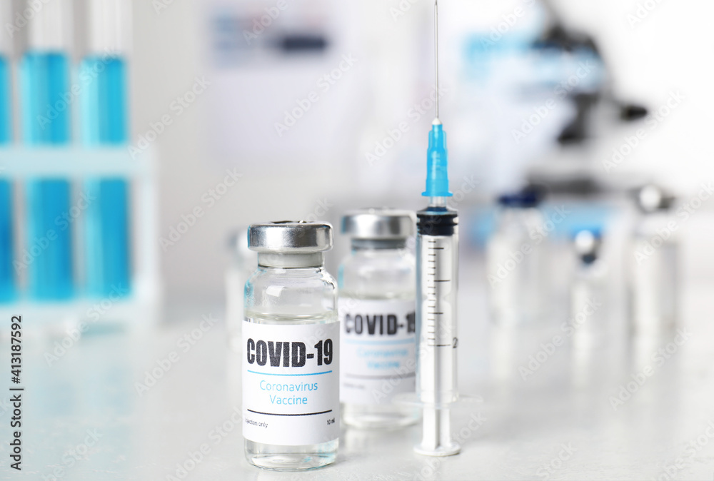 Vials with vaccine against Covid-19 and syringe on white table indoors Vials with vaccine against Covid-19 and syringe on white table indoors