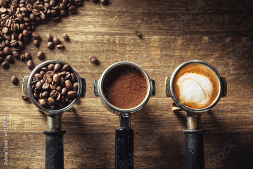 Coffee in its various forms from raw beans to ground coffee and cappuccino in three portafilters on a rustic wooden background photo