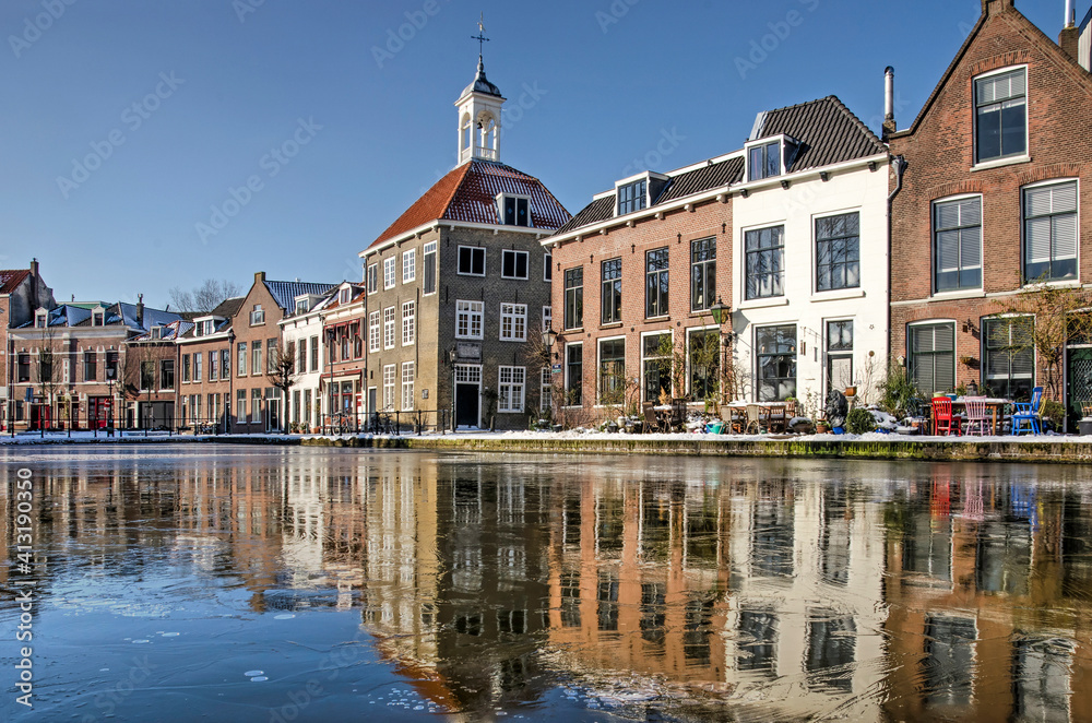 Schiedam, The Netherlands, February 11, 2021: the historic Bag Carriers House and other historic brick and plaster buildings reflecting in the frozen river Schie