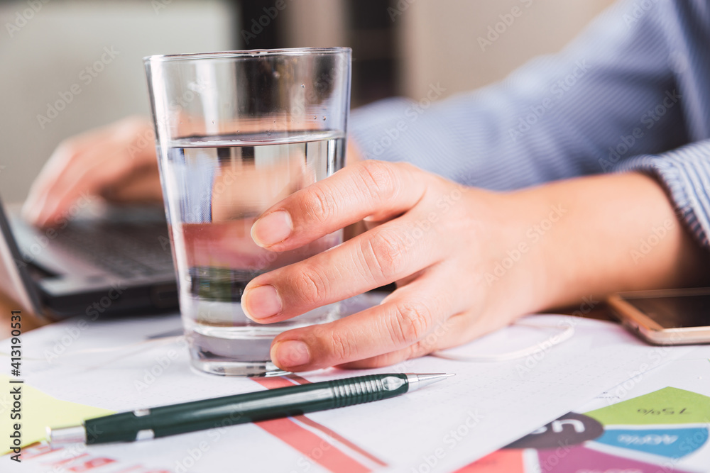 Close-up of a businesswoman using her laptop at the office desk, with a glass of water. Close-up of a businesswoman using her laptop at the office desk, with a glass of water.