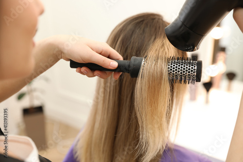 Stylist drying client's hair in beauty salon, closeup