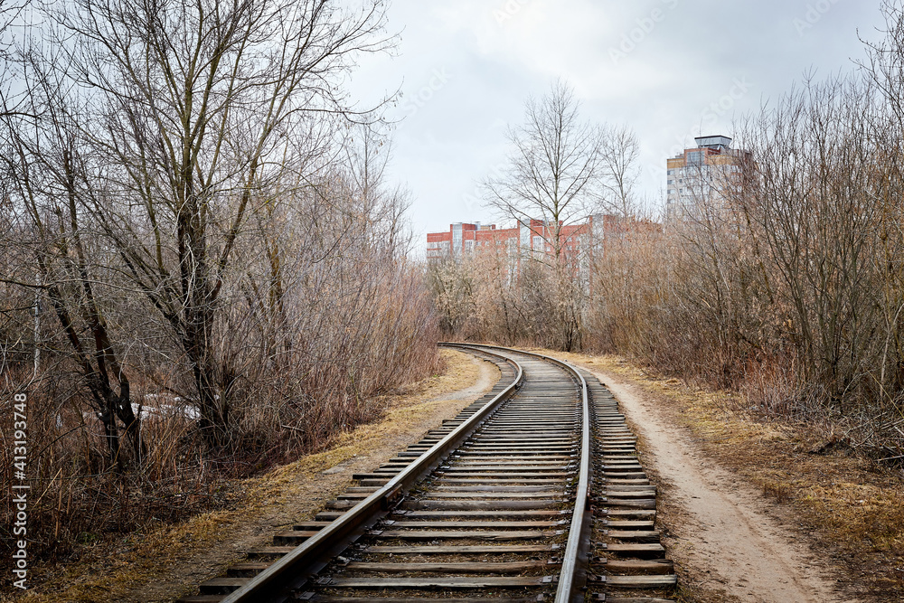 A railway running to the city and large houses among bare and bald trees on an autumn or spring day A railway running to the city and large houses among bare and bald trees on an autumn or spring day