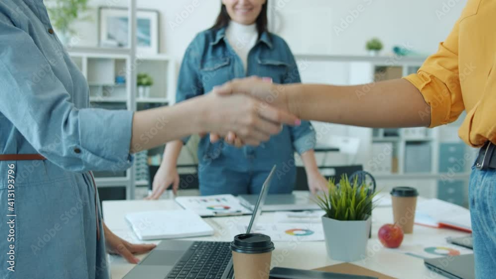Slow motion low shot of unrecognizable mixed race women sharking hands expressing cooperation and unity in office. Togetherness and collaboration concept. Slow motion low shot of unrecognizable mixed race women sharking hands expressing cooperation and unity in office. Togetherness and collaboration concept.