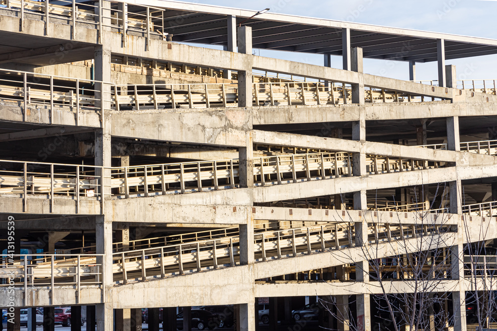 Gray concrete multi-storey parking garage for cars and staircase is outside in winter in a sunny day