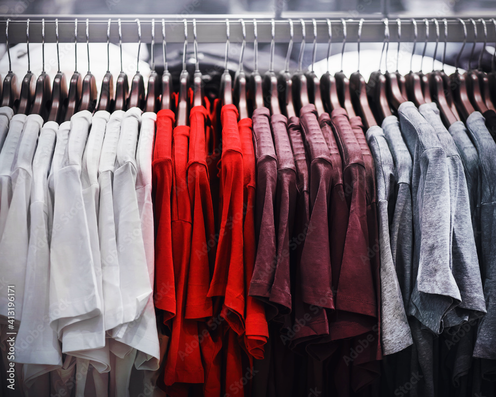 Simple casual T-shirts in different colors and sizes hang on hangers in a clothing store in the mall. Shopping.