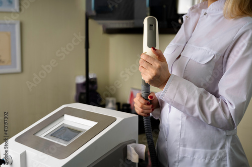 cosmetologist doctor in a white coat, next to a laser device for tattoo, permanent, hair removal, peeling, with a handpiece in his hands