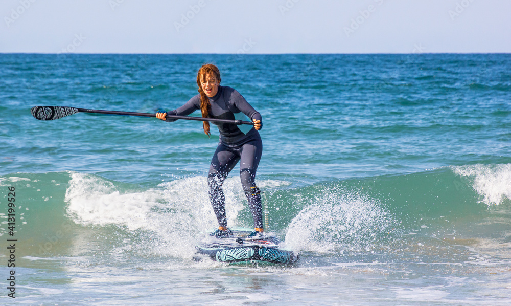 Young woman with wetsuit swimming on stand up paddle board. Water sports , active lifestyle. SUP surfer woman caught the wave. Surfing on inflatable SUP stand-up paddle board in winter. Surf course Young woman with wetsuit swimming on stand up paddle board. Water sports , active lifestyle. SUP surfer woman caught the wave. Surfing on inflatable SUP stand-up paddle board in winter. Surf course