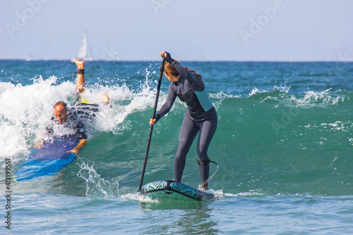 Young woman with wetsuit on an inflatable paddle SUP surfboard preparing to take the wave. Funny scene at sea. man in a wave. Water sports , active lifestyle