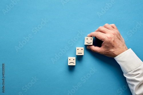 Businessman hand arranging or choosing happy face symbol on wooden cubes. Increase in customer service evaluation and satisfaction survey