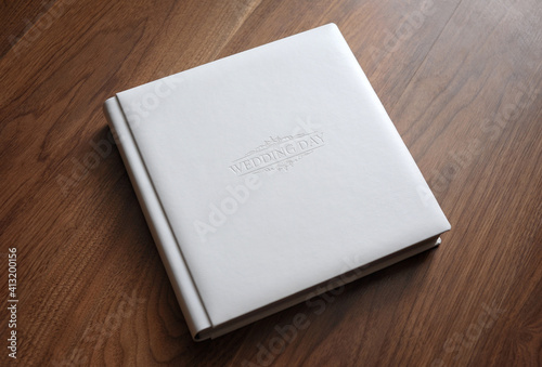 White leather wedding photo album with embossed cover lies on a wooden table