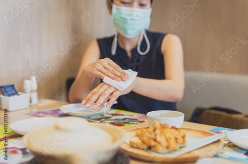 Woman in medical mask cleaning her hands with a wet wipes in restaurant.