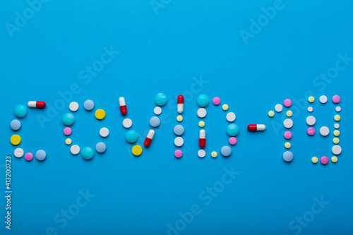 Word Covid 19 wrote with multicolored pills on blue background with free space for text. Concept of prevention from virus agitation to make a vaccine.