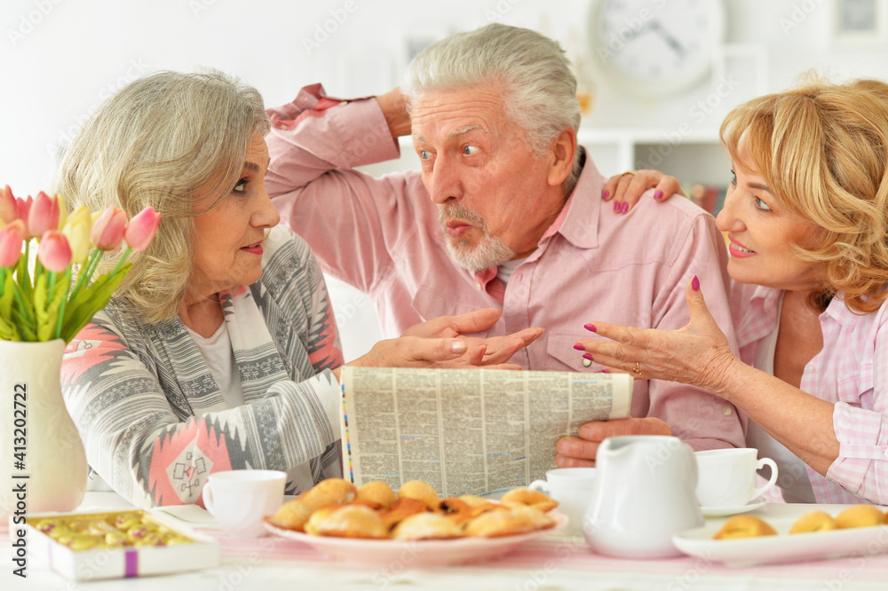 happy Senior people reading newspaper while drinking tea with cookies at kitchen happy Senior people reading newspaper while drinking tea with cookies at kitchen
