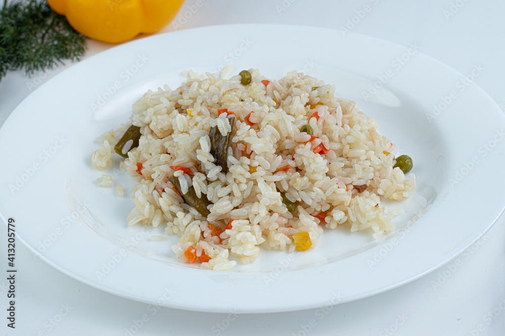 Cooked rice with vegetables on a light background in a white plate.