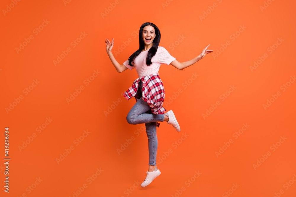 Full length profile photo of cheerful nice lady jumping hands sides beaming smile isolated on orange color background