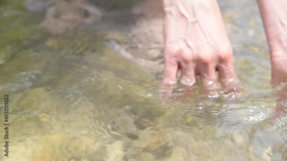 A woman touches the water of a river with her hand. Feeling the water of a river. A woman dipping sun hands in the river water A woman touches the water of a river with her hand. Feeling the water of a river. A woman dipping sun hands in the river water