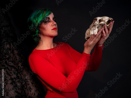 Girl dressed in red on bear skin thinks to be or not to be holding a sheep skull in her hands 