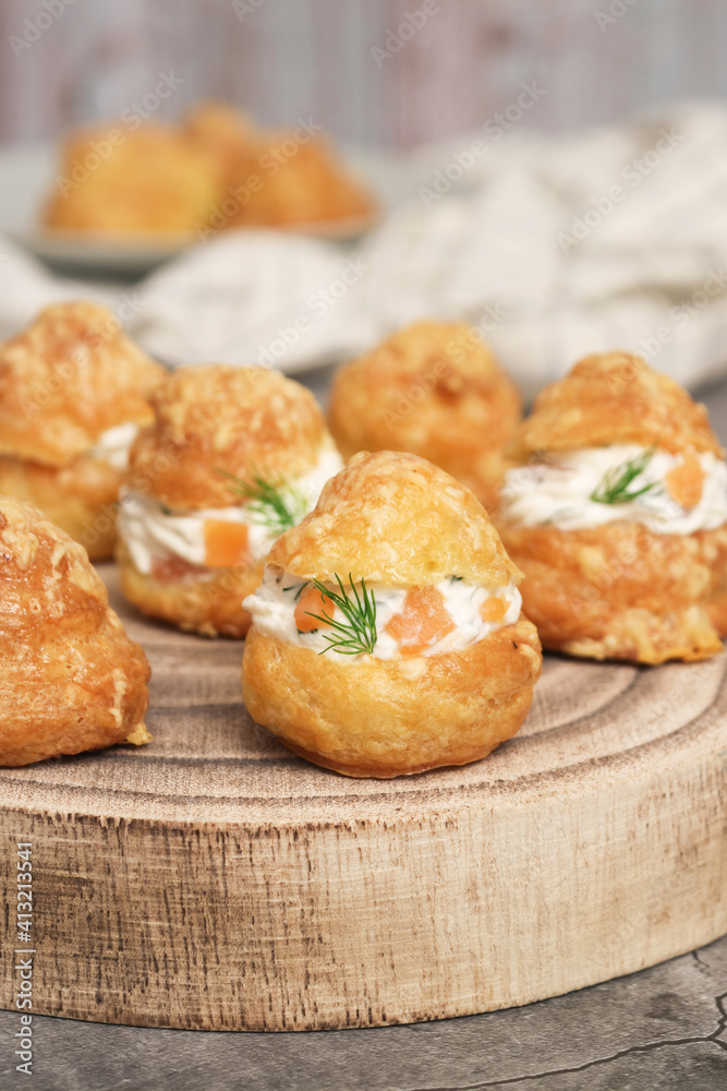 A traditional French savory choux dough cheese puff filled with fresh cheese mixed with smoked salmon in a wooden plate decoration with dill leaf. Pastry know as typically Burgundy serve as appetizer