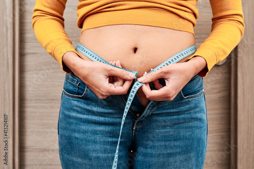 Front view of unrecognizable woman measuring her waist circumference with a tape measure. Concept of diet and weight control.