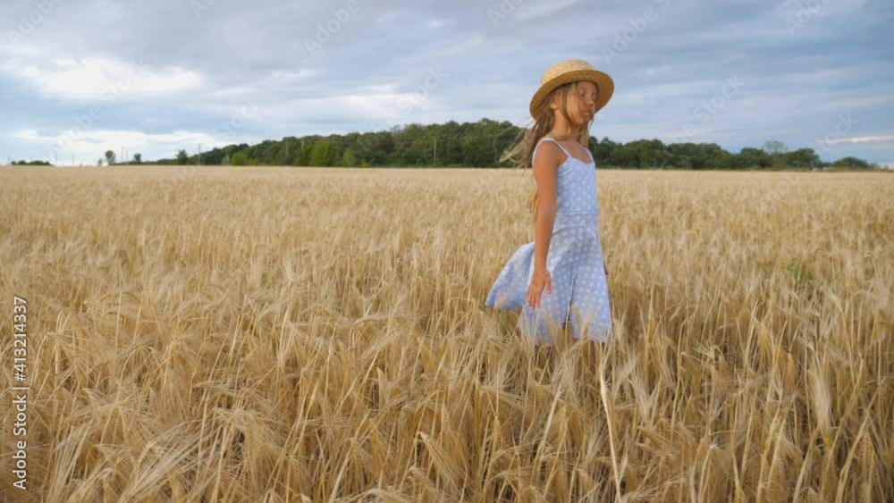 Close up of beautiful small girl with long blonde hair walking through wheat field. Cute child in straw hat touching golden ears of crop. Little kid in dress going over the meadow of barley.Dolly shot Close up of beautiful small girl with long blonde hair walking through wheat field. Cute child in straw hat touching golden ears of crop. Little kid in dress going over the meadow of barley.Dolly shot