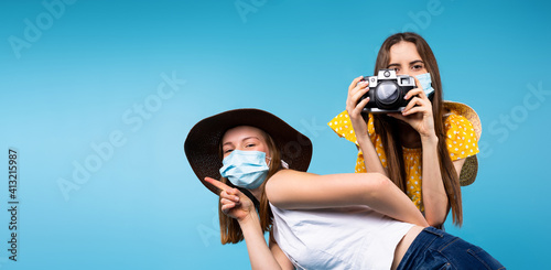 Banner,long format. Happy female friends taking pictures and posing in summer clothes, hat and medical mask on blue background with side space. © Viorel