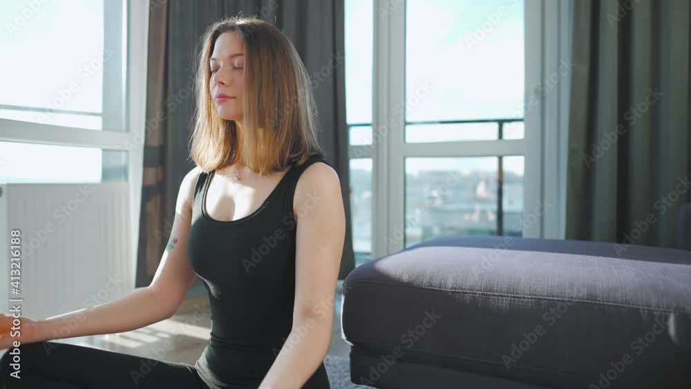 Young caucasian woman in black jumpsuit sitting in lotus position and meditating, yoga at home. Slow motion Young caucasian woman in black jumpsuit sitting in lotus position and meditating, yoga at home. Slow motion