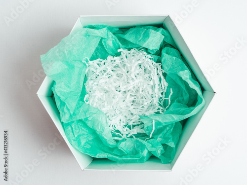 Open a hexagonal white gift box with green wrapping paper inside and shredded white paper. Mockup.