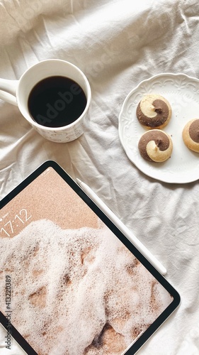 A cup of coffee on a bed with cookies and a tablet. Morning 