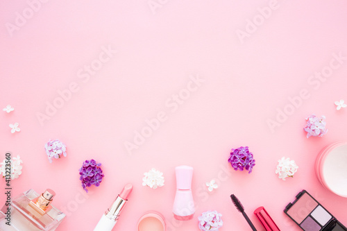 Various decorative makeup cosmetics and fresh cherry blossoms on light pink table background. Pastel color. Different beauty essentials for women. Empty place for text or logo. Top down view. Closeup.