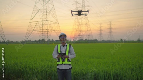 An electrical engineer forcing a drone To inspect high voltage poles before starting a project Assigned by the organization during the sunset time
