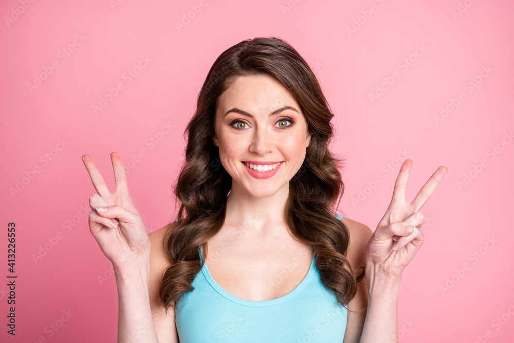 Close up portrait of curly lady show two hands finger v-sign blue tank-top isolated on pastel pink color background Close up portrait of curly lady show two hands finger v-sign blue tank-top isolated on pastel pink color background