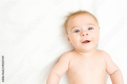 Happy newborn baby boy with a big smile. Adorable baby lying on white background, copy space. Funny child infant with blue grey eyes and ginger hair looking at camera