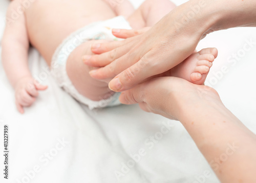 Woman hands doing legs massage to newborn. Massage for little baby. Close-up of the small baby leg on a white background