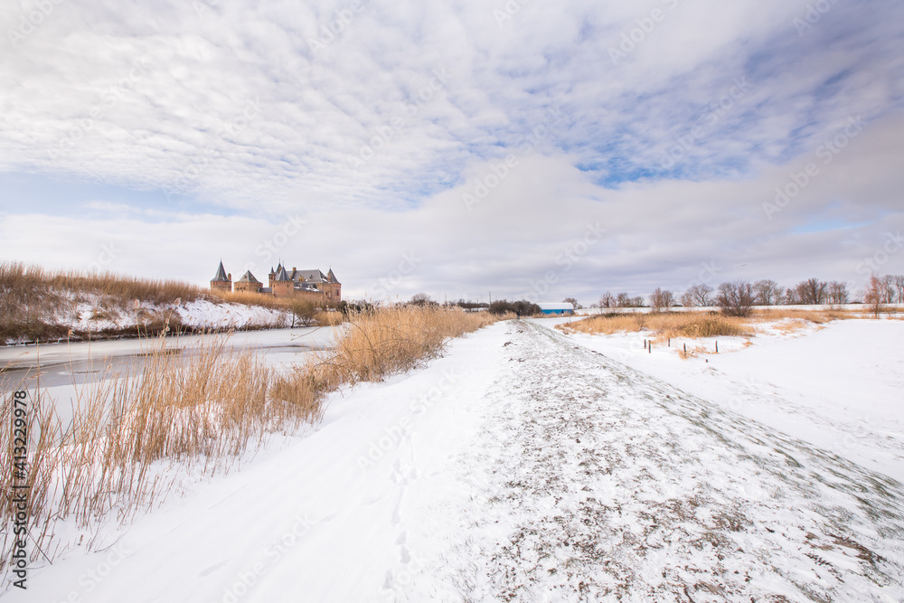Winter Dutch landscape with a frozen canal, dike with ice, snowy landscape and the fairy tale-like medieval castle of Muiderslot