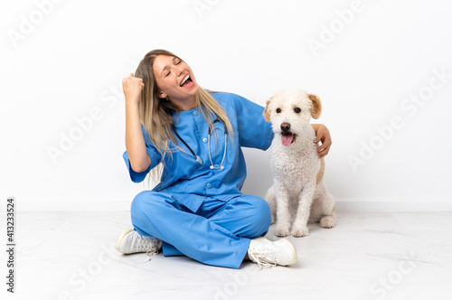 Young veterinarian woman with dog sitting on the floor celebrating a victory