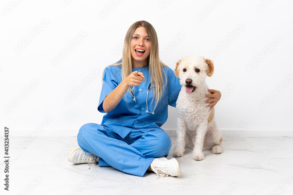 Young veterinarian woman with dog sitting on the floor surprised and pointing front Young veterinarian woman with dog sitting on the floor surprised and pointing front