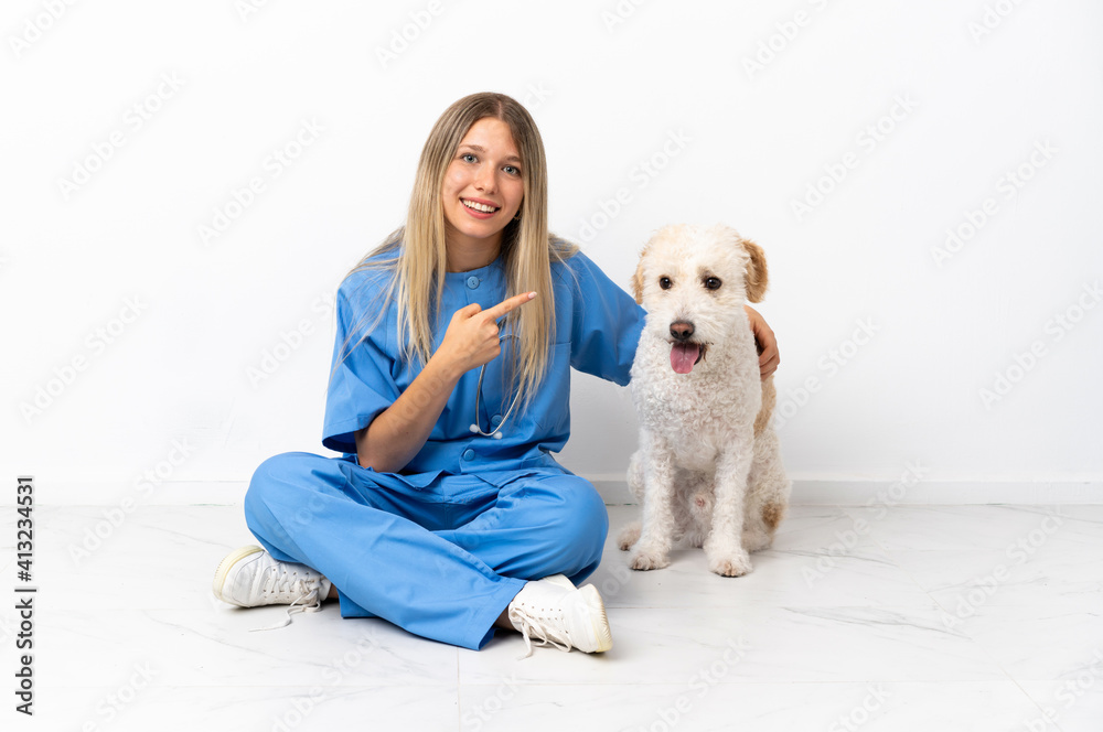 Young veterinarian woman with dog sitting on the floor pointing to the side to present a product Young veterinarian woman with dog sitting on the floor pointing to the side to present a product