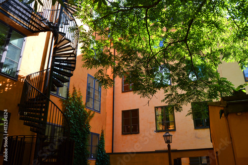 Cozy courtyard of the orange house in the Old Town of Stockholm. The sun's rays shine through the green leaves of the tree. Summer in Sweden.
